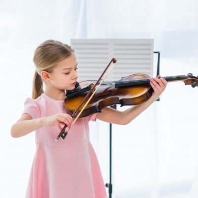 cute little child in pink dress playing violin at home